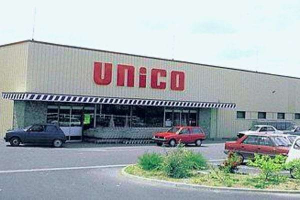 Supermarché Unico avec son enseigne rouge et une marquise à rayures noires et blanches.