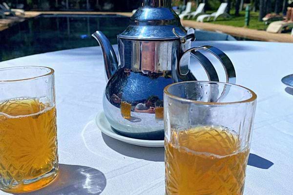Deux verres de thé marocain sur une table avec piscine en arrière-plan.