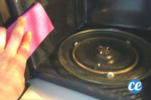 Main tenant une éponge rose, nettoyant l'intérieur d'un micro-ondes après le traitement au citron.