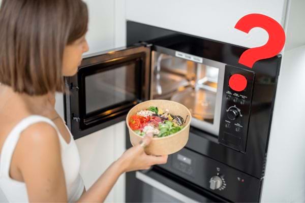 Femme hésitante avec bol, devant micro-ondes, icône question rouge.