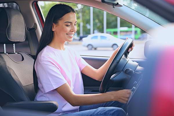 Une femme souriante au volant de sa voiture.