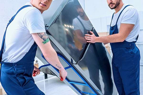 Deux déménageurs avec harnais et chariot soulèvent un grand écran plat.