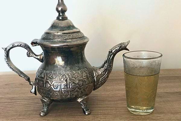 Théière marocaine en argent à côté d'un verre de thé sur une table en bois.