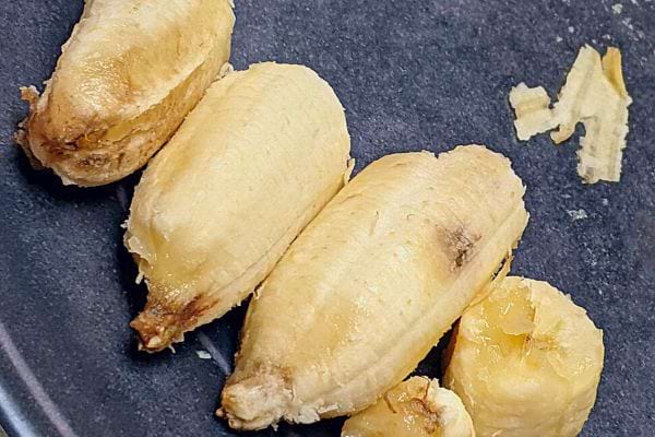 Plusieurs morceaux de banane jaune coupée sur une assiette grise.
