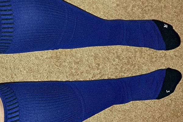 Jambes avec bas de contention bleu sur moquette vue de dessus.