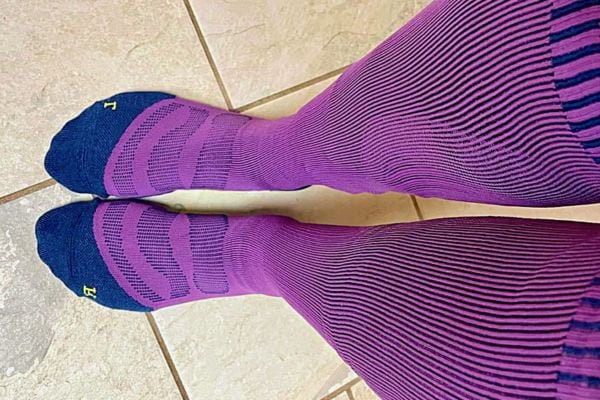 Deux jambes avec bas de contention violet sur sol en carrelage.