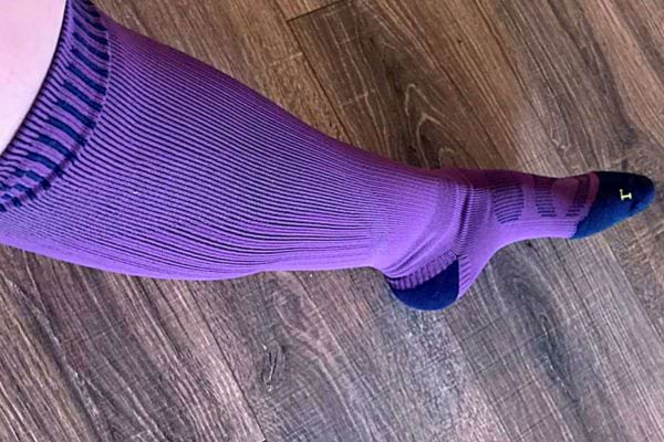 Jambe avec bas de contention violet sur sol en bois.