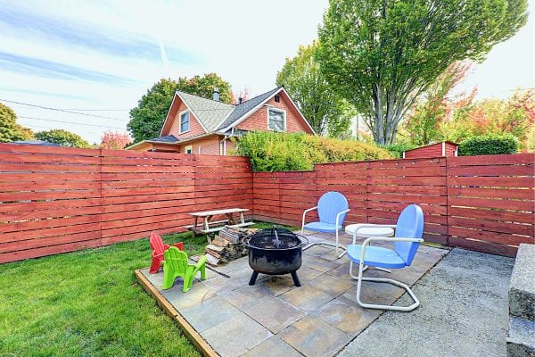 Cour arrière avec clôture en bois rouge, feu de camp, chaises bleues et blanches et jouets pour enfants.