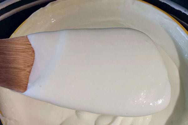 Une cuillère en bois soulevant du mascarpone blanc crémeux dans une casserole.