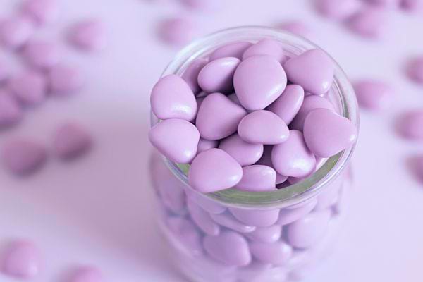 Des dragées violettes en forme de cœur dans un pot en verre transparent.