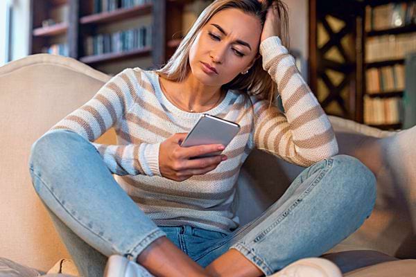 Femme frustrée vérifiant son téléphone sur le canapé.