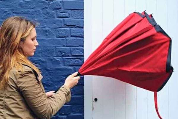 Une femme lutte contre un parapluie rouge renversé par le vent.