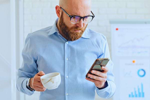 Homme chauve perplexe regardant son téléphone avec café.
