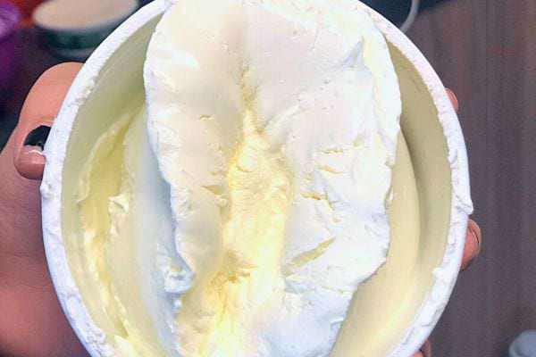 Une main tenant un pot de mascarpone ouvert, montrant sa texture épaisse et onctueuse.