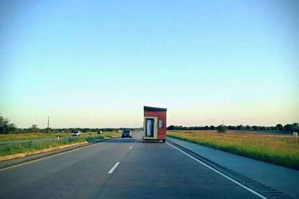 Petite maison sur remorque roulant sur une autoroute, vue de l'arrière.