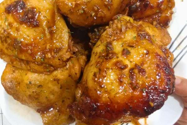 Des cuisses de poulet marinées et brillantes sur une assiette, avec une peau prête à devenir croustillante à la cuisson.