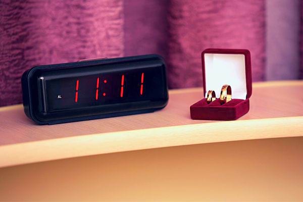 Réveil digital affichant "11:11" à côté d'une boîte de bague, évoquant le romantisme.
