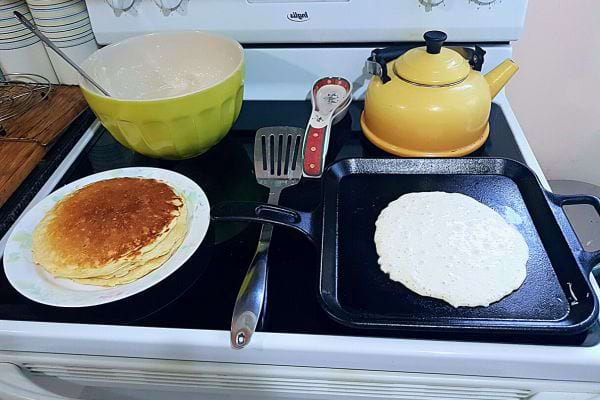 Pancakes dorés sur une poêle, avec une pile à côté.