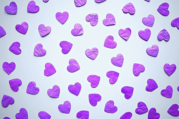 Plusieurs cœurs violets en papier éparpillés sur un fond blanc.