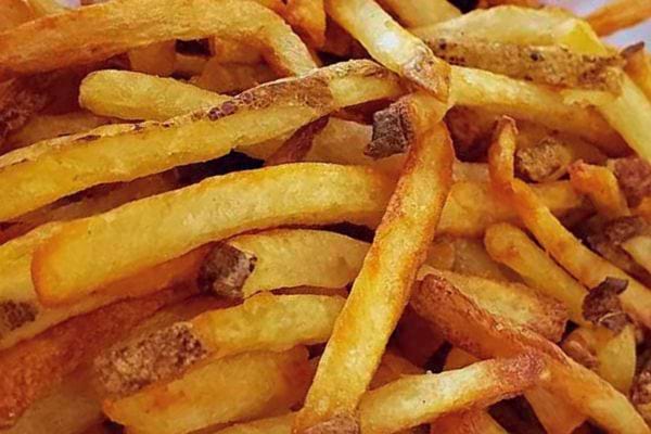 Une multitude de frites dorées et fines s'étalent sur une surface, probablement prêtes à être servies.