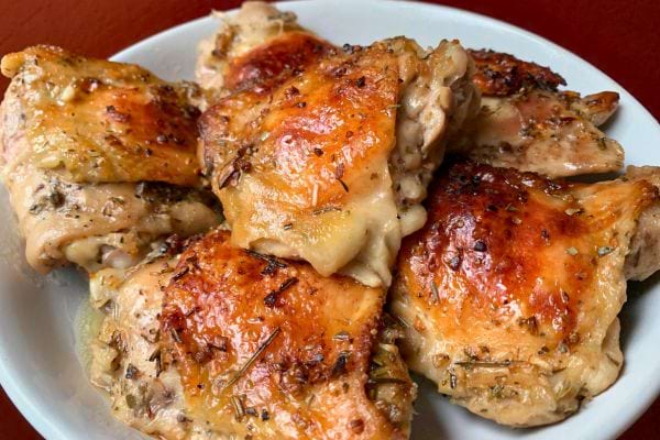 Des cuisses de poulet rôties dorées reposant sur une assiette blanche, avec la peau croustillante.