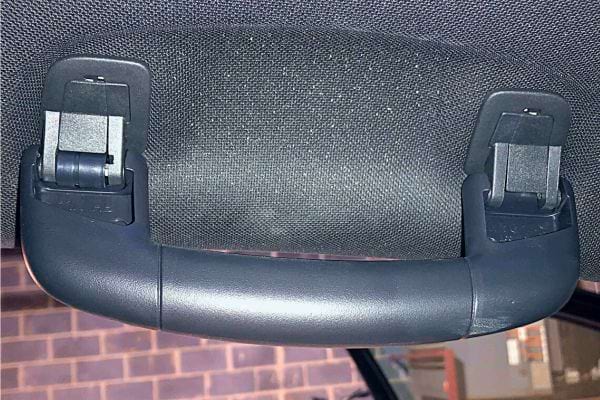 Gros plan sur une poign&eacute;e de maintien int&eacute;rieure de voiture avec attaches visibles.