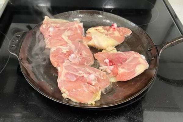 Des cuisses de poulet crues dans une poêle sur une cuisinière électrique, prêtes à être cuites.