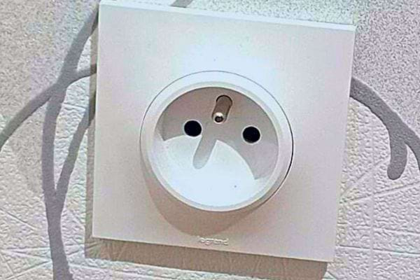 Une prise électrique murale avec un trou de terre ressemblant à une expression de surprise