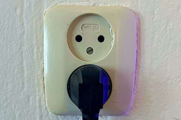 Ancienne prise beige avec une fiche noire branchée, le trou de terre supérieur formant un visage triste.