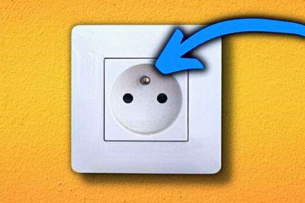 Prise murale blanche avec un trou de terre en haut, signalée par une flèche bleue, sur un fond jaune.