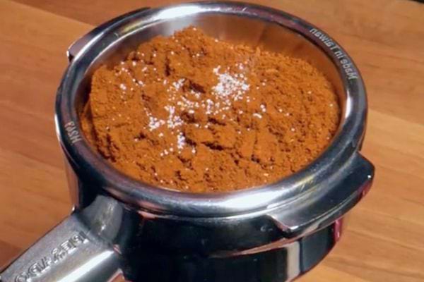 Du sel éparpillé sur du café moulu dans un porte-filtre d'une machine à espresso sur un plan de travail en bois.