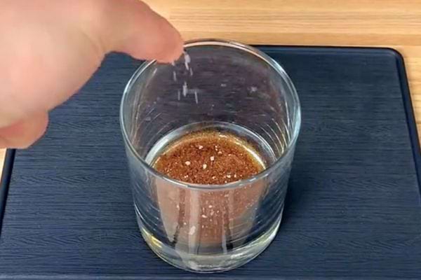 Des grains de sel tombant dans un verre contenant un café brun transparent sur un plateau bleu.