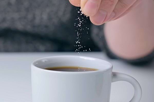 Une main saupoudrant du sel dans une tasse de café noir.