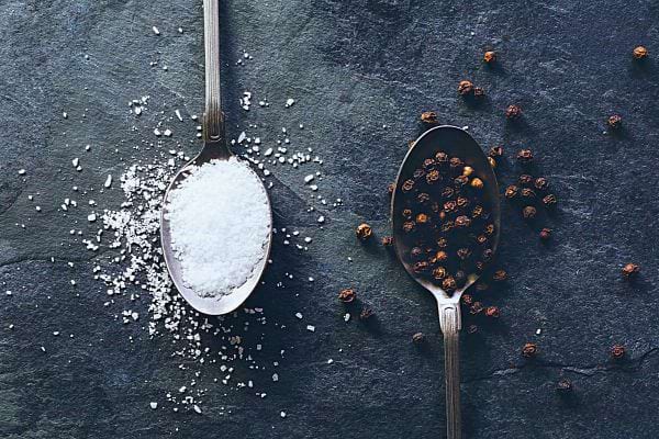 Sel fin dans une cuillère, avec des grains de poivre à côté.
