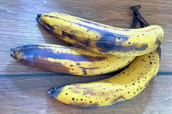 Trois bananes mûres avec des taches brunes sur une surface en bois.