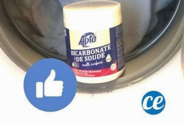 Main tenant un pot de bicarbonate devant une machine à laver ouverte.