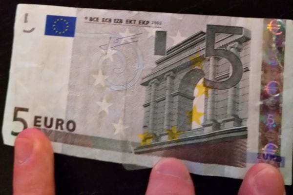 Ein 5-Euro-Schein in der Hand deutet auf eine finanzielle Überraschung hin.