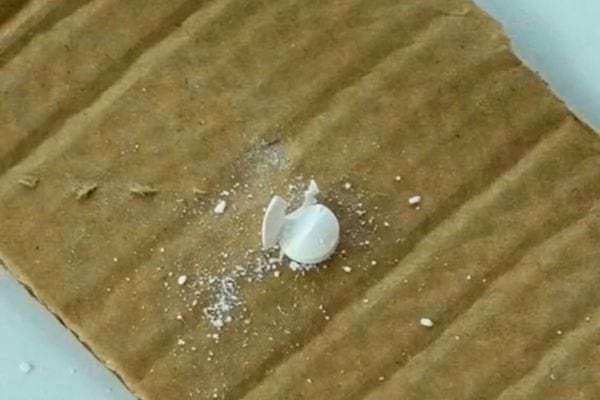 Comprimé brisé en morceaux sur un morceau de carton brun.