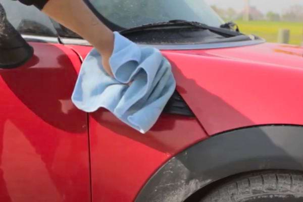 Nettoyage de la carrosserie rouge d'une voiture avec un chiffon bleu.