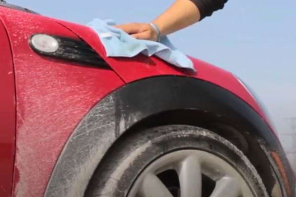 Main d'une personne nettoyant la carrosserie rouge d'une voiture avec un chiffon.