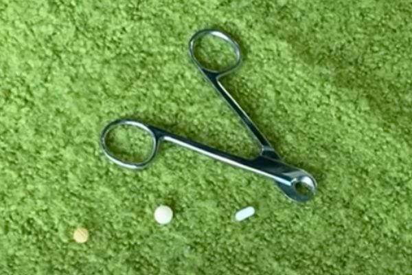 Coupe-ongles métallique sur une surface en tissu vert avec un comprimé à côté.