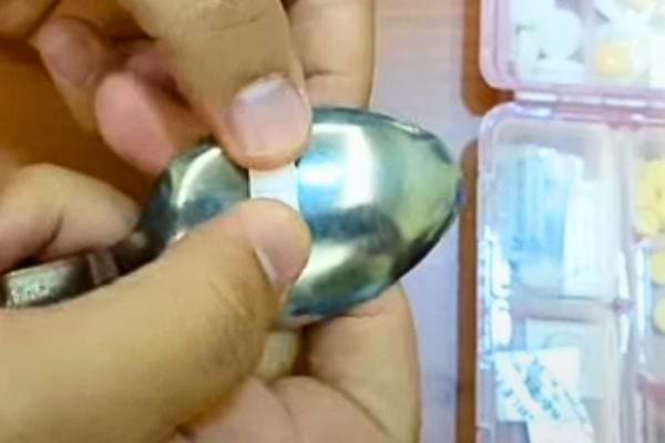 Comprimé placé sur le dos d'une cuillère métallique, tenu par des doigts, prêt à être coupé.