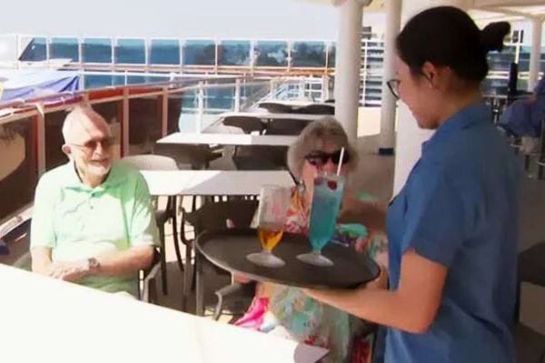 Couple &acirc;g&eacute; recevant des cocktails de la part d'une serveuse sur le pont du navire.
