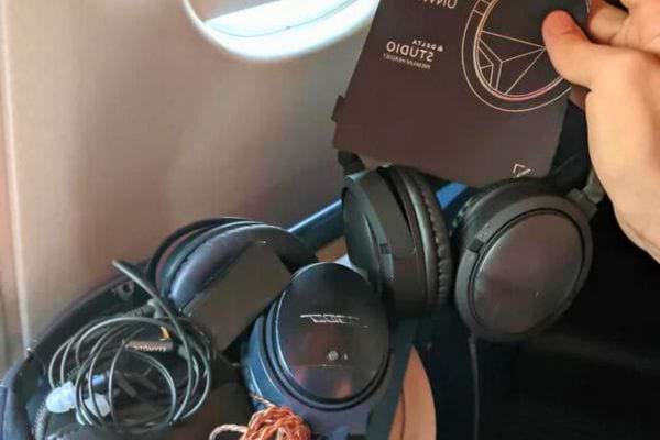 Deux casques audio noirs dans un avion, l'un tenu par une main.