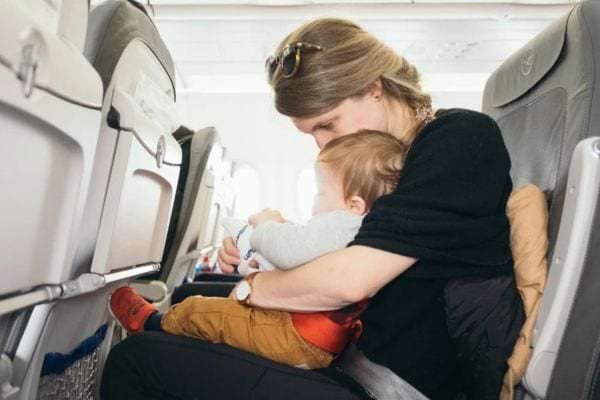 Une femme blonde tient un bébé dans ses bras à bord d'un avion.
