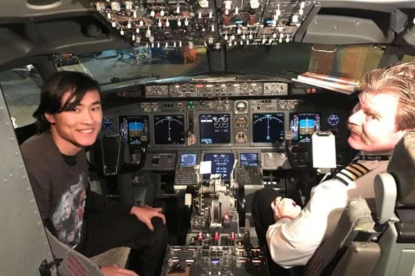 Un homme asiatique est assis dans le cockpit d'un avion à côté du pilote, tous deux souriants.