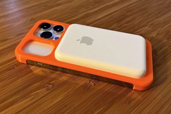 Un iPhone avec une coque orange et une batterie MagSafe blanche attachée, posé sur une table en bois.