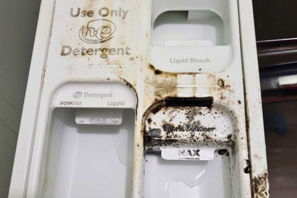 Un bac à détergent de machine à laver, avec des taches de saleté et des traces de moisissures.