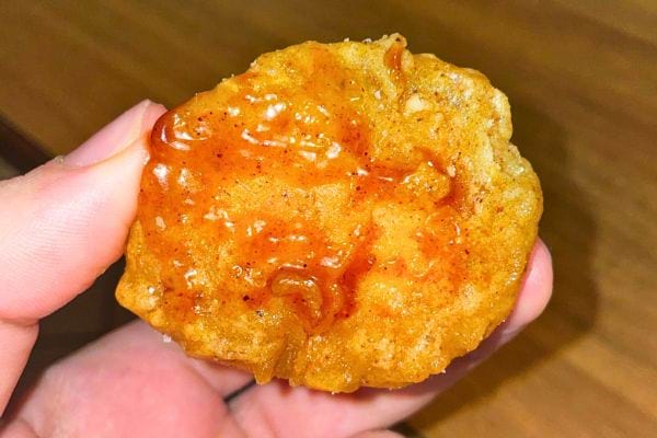Un nugget de poulet brillant de sauce tomate tenu à la main.