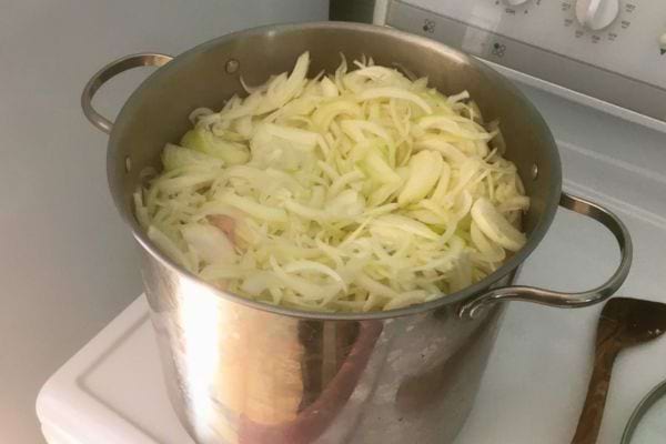 Grand volume d'oignons émincés dans une casserole en inox, prêt pour la cuisson.